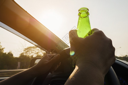 男司机妇女驾驶汽车时持有啤酒瓶的妇女一种高清图片