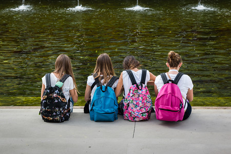 一群坐在河边背着书包的女生背面背景图片