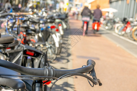 荷兰在阿姆斯特丹的自行车泊停放日荷兰阳光在Bike泊车场和一对夫妇骑自行车者与两辆赛手一起离开关注焦点的SunnyDay停車處健街道高清图片素材