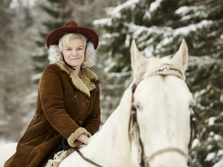 辔户外穿着冬季夹克和帽子的迷人女骑着白马望摄像机看她的眼睛接触图片