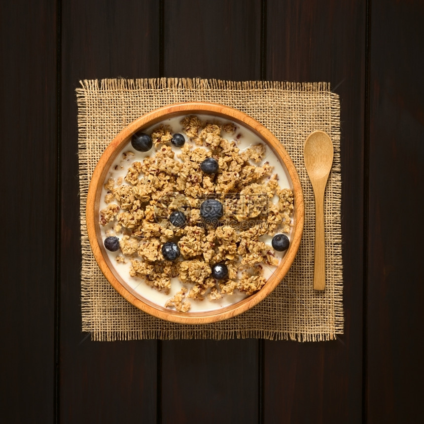 面带新鲜蓝莓和木碗中的牛奶用自然光照着黑木头上方的灯光照相以鲜蓝浆果和奶粉装在木碗中制的加糖乳品图片