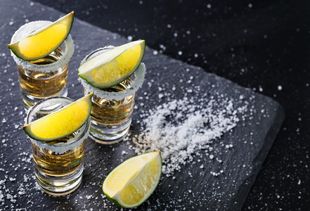 墨西哥传统喝的龙舌兰酒杯圆边和石灰上含盐的龙舌兰杯黑底酒精鸡尾墨西哥传统饮料桌子水果酒吧背景图片