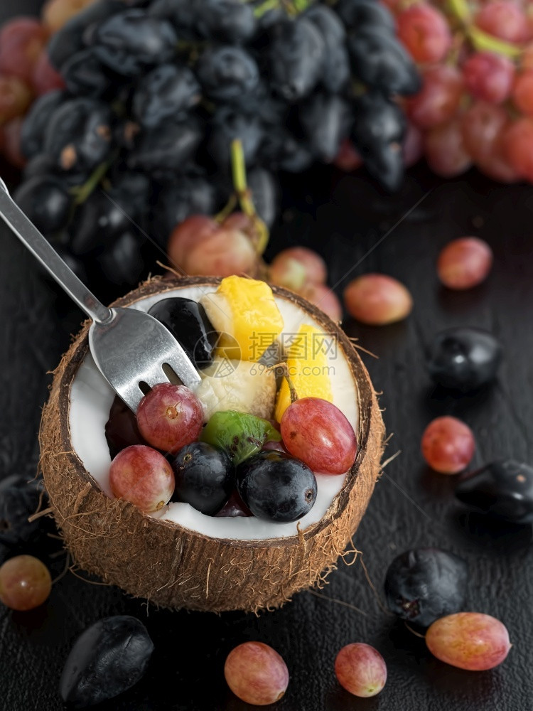 新鲜水果位于本底椰子葡萄团的半块椰子中水果位于黑石板上半椰子黑质石头背景健康营养素食物等半块椰子上红色的素食主义者甜图片