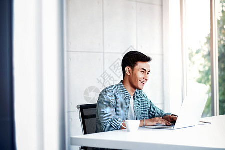 自信的快乐青年商人在办公室用电脑笔记本上工作办公桌旁临时服人穿自己的图片