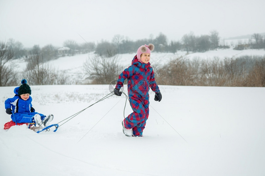 滑动姐快乐的男孩和女在冬天从山上拉雪橇冬季户外运动会寒假快乐的男孩和女在冬天从山上拉雪橇冬季户外运动会公园图片