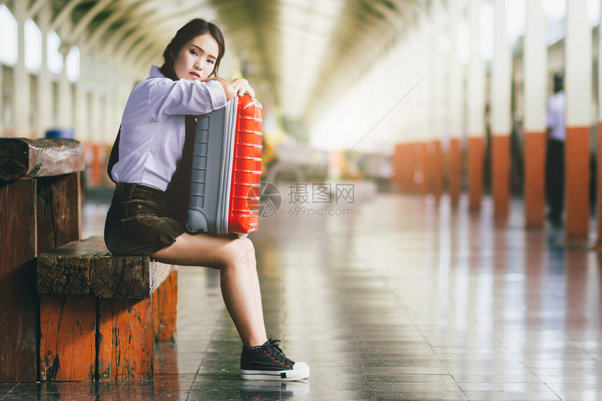 在火车站旅行时亚洲怀孕妇女旅行者坐在火车站的与一个红色手提箱起等待户外美丽的女图片