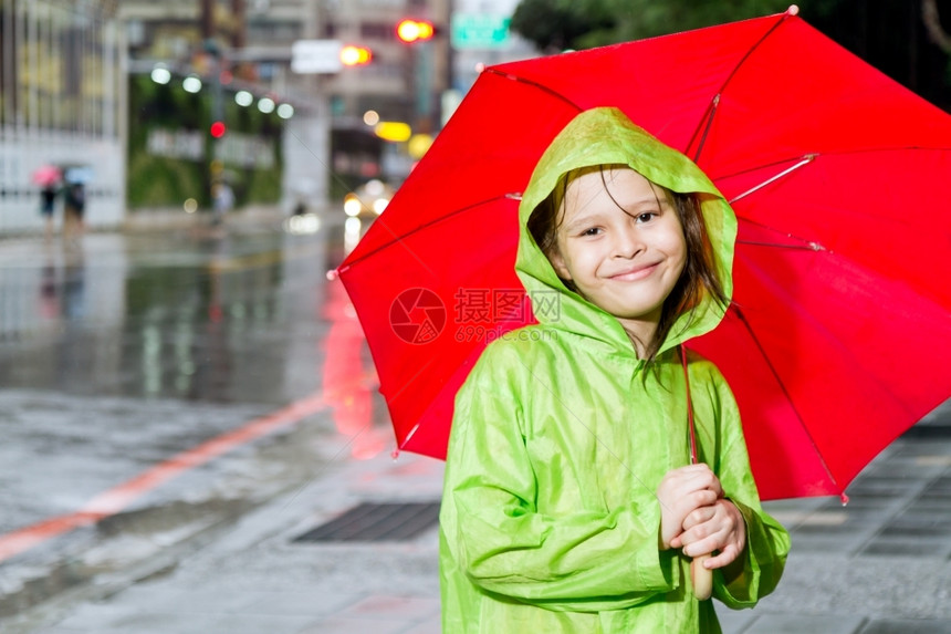 穿着绿色雨衣在街对面人行道上拿着红伞的雨中女孩下天气漂亮的图片