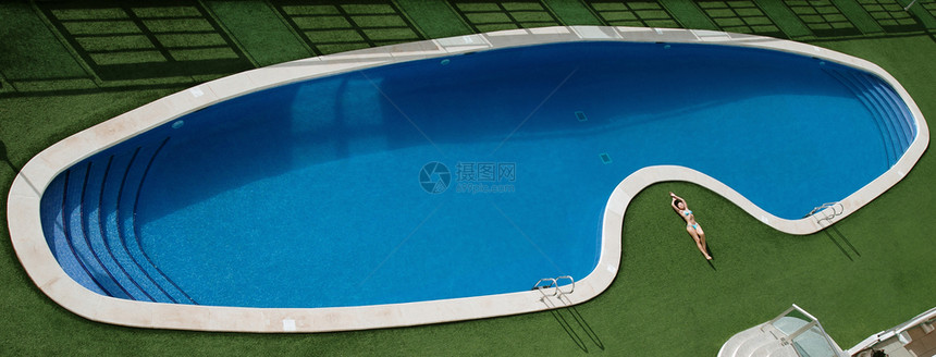 比基尼美女躺在游泳池附近的绿草地上晒日光浴图片