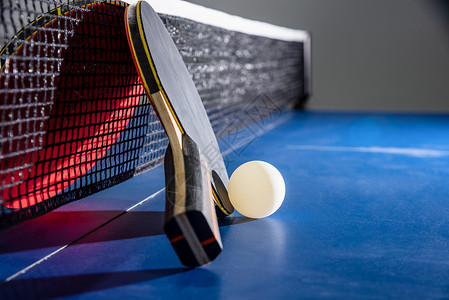 乐趣桌子特写黑色和红乒乓球拍在蓝台上用网拍一个白球乒乓拍是一种运动竞赛设备室内活动和运概念背景特写红色乒乓球拍白和网色的背景图片