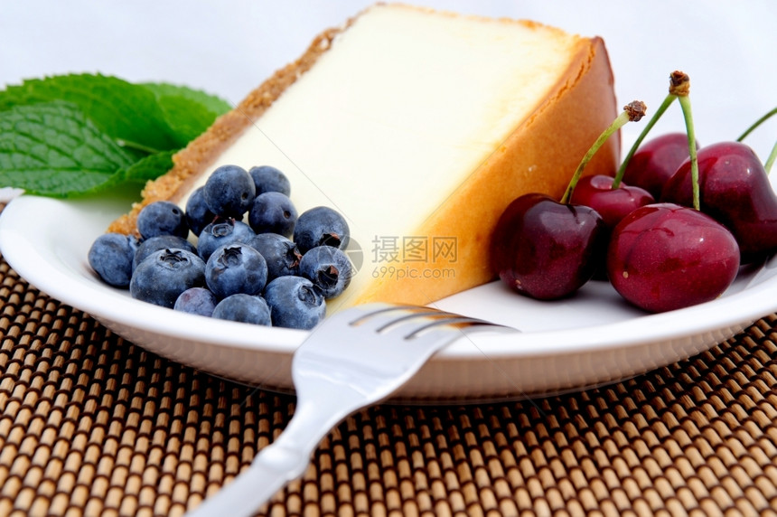 白色的起司季节水果配有一片平芝士蛋糕和薄荷叶的美食在白碟蓝莓和红樱桃奶酪蛋糕樱桃和蓝莓面包店图片