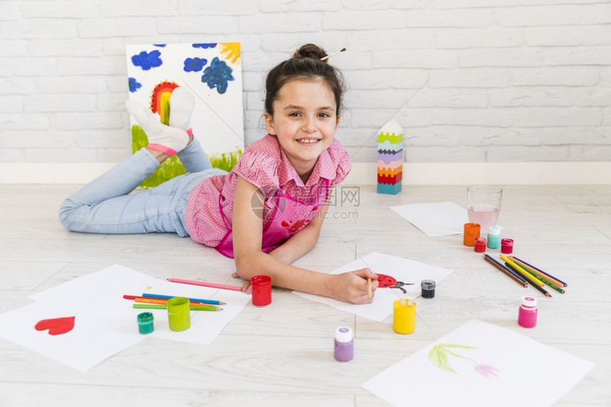 美丽面带油漆刷白纸的躺在地板上画着微笑的小女孩有创造力的活动图片