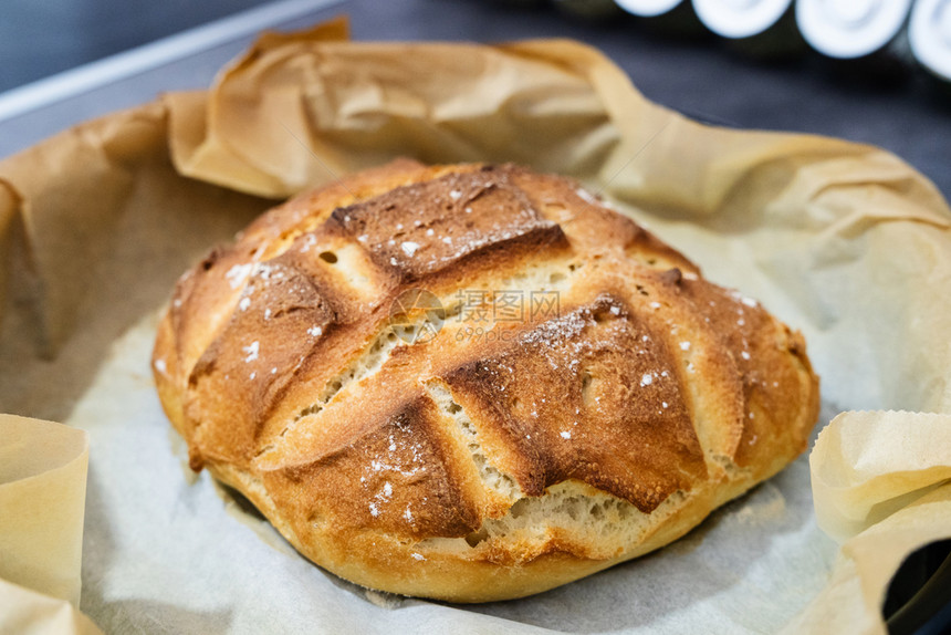 脆皮静物紧贴在新鲜烘烤的土制自面包上锅炉菜里的传统生锈面包饼在烤纸上白色的图片