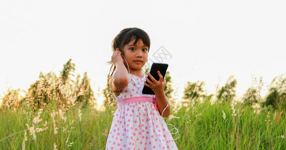 成人亚洲女童听手机的音乐和歌唱夏天在草地上欢乐自然而女孩人类图片