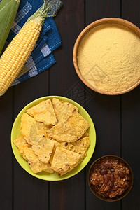 面粉玉米饼用玉米粉cobs和一小碗辣椒卷心菜盘子上自制烤玉米薯片用天然光照在黑木头上的片营养自然小吃背景