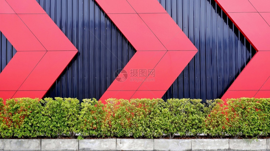 丰富多彩的外部建筑装饰设计概念中绿色灌木墙后面黑金属板壁上的红箭头紧色图案合成的泰国图片
