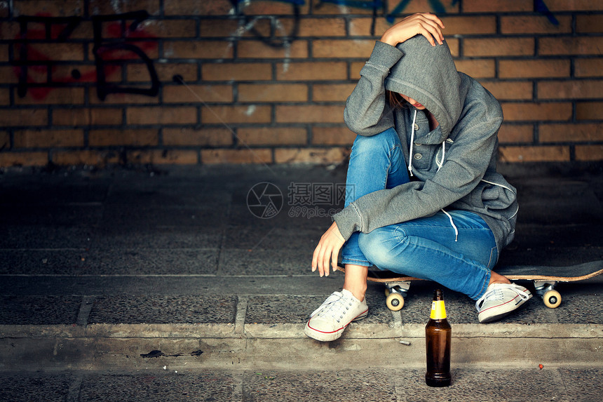 一种不良孤独的少女坐在黑暗门道上啤酒瓶装着汗衫和兜帽随意的图片