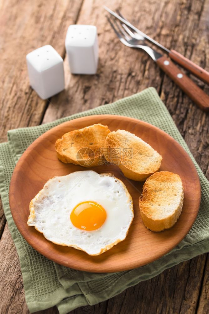 黄色的早午餐一个新鲜的煎蛋阳光明亮一面边上加烤包饼片放在木板餐具盐和胡椒在后面的选择焦点中专注鸡蛋前与烤面包白质图片