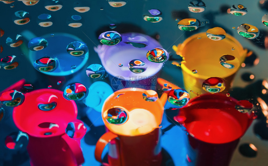 多色抽象背景通过玻璃查看在模糊的多彩水罐和桶上放满一滴液体选择对前景地多彩抽象背的聚焦通过滴子进行选择对前景地多彩抽象背的聚焦气图片