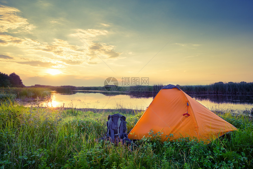 假期河旅行橙色帐篷和在日落时湖边的背包黄昏时湖边的橘色帐篷和背包图片