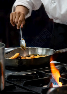 制造厨师在房炉灶的煎锅中用火焰做饭手油炸图片