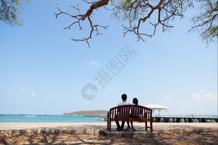 情侣旅行坐在树下长凳上的夫妻海前的浪漫夫妇人行道图片