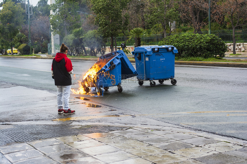 外部雅典市示威活动结束后一名女孩正在寻找着火烧毁的垃圾桶热灾难图片