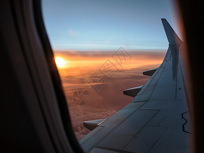 望着一架飞机的窗外白色飞机翼和日落在云层上的日落方天空飞机场腰带图片