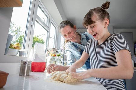 玩面团女人社会的母亲和女儿在厨房里玩得开心为家用烤面包一起做饭自己教学背景
