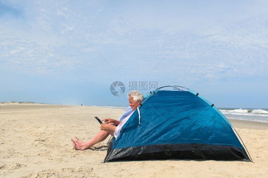 单身老人在海滩的避难所内有数字石板露营药片荷兰互联网图片