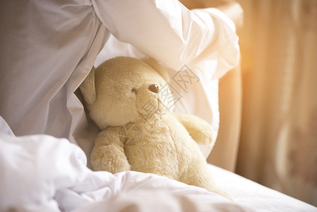 迷人的黑发女郎坐在床上穿着白色衬衫睡衣带着她的棕色泰迪熊吸引人的挑衅晒黑背景图片