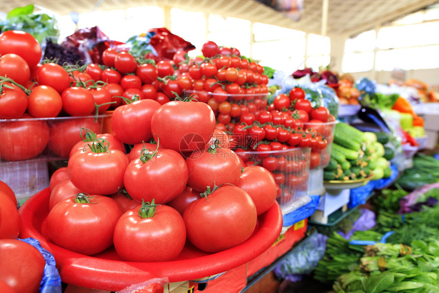 质地背景中不同品种的成熟红番茄在市场上的托盘中出售黄瓜菠菜和其他蔬模糊不清市场上出售的西红柿黄瓜菠菜和其他蔬束不同的图片