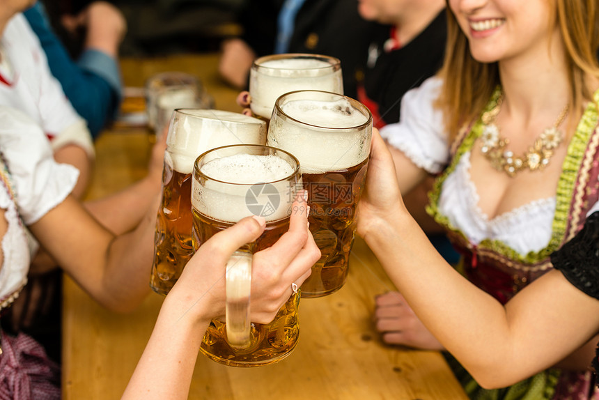 斯坦少女装快乐的穿传统Dirndl服装的巴伐利亚女孩喝啤酒在Oktoberfest巴伐利亚女孩喝啤酒时玩得开心图片