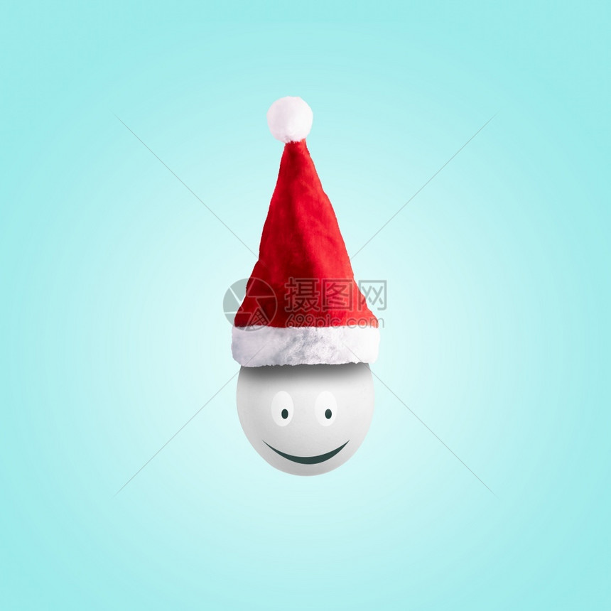 季节冬天圣诞快乐的节概念在淡蓝色背景下以圣塔帽戴着微笑的鸡蛋可爱图片