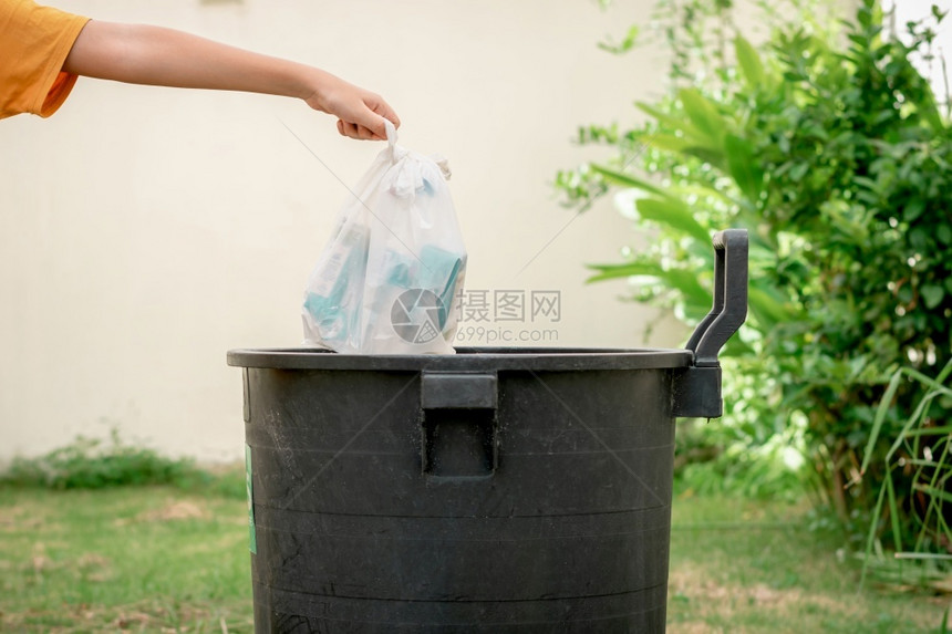 人类绿色保护手把垃圾扔进塑料袋花园的垃圾桶图片