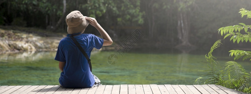 荒野男孩坐在木桥上度假旅行中享受看森林的观光男生假期图片