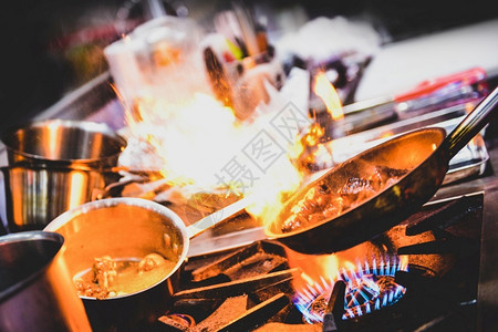 商业的油厨师在房炉灶的煎锅中用火焰做饭盘子背景图片