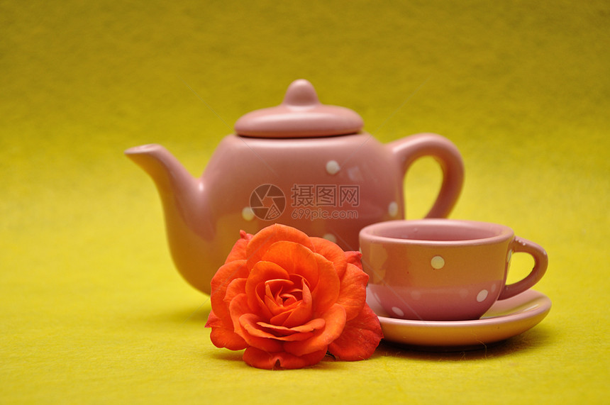 新鲜的自然陶瓷制品茶杯和水壶黄色背景的橙玫瑰图片