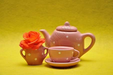 餐具瓷放茶杯和水壶黄色背景的橙玫瑰图片