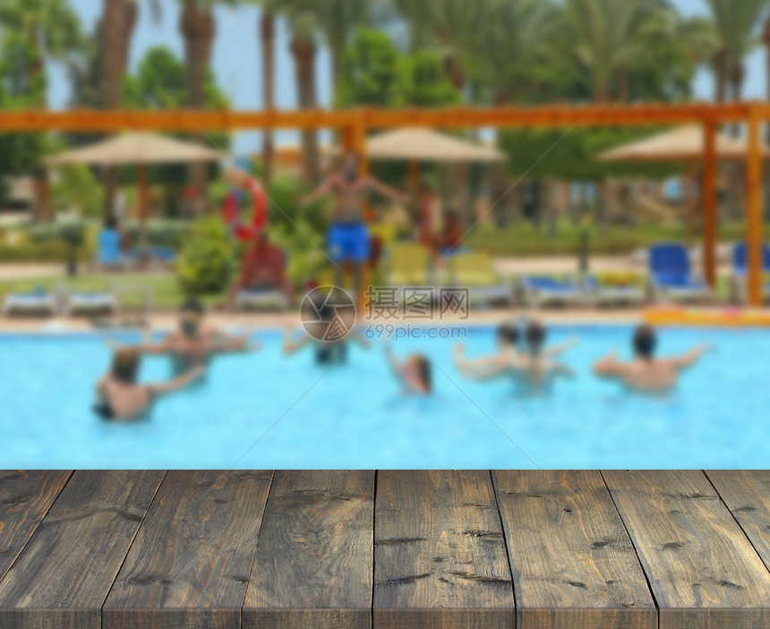 复古木板可欣赏热带派对游泳池中跳舞的女桌面与放松的人复古木板们在现代热带度假村放松棕榈桌上移动