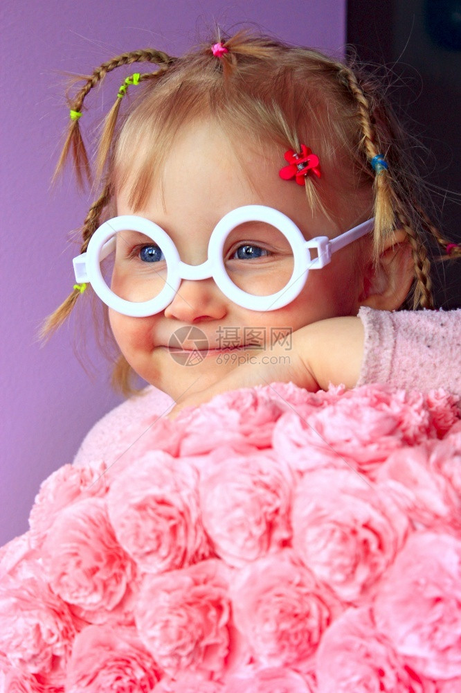 魅力白种人太阳戴塑料眼镜的小女孩在用纸浆制成的花旁微笑图片