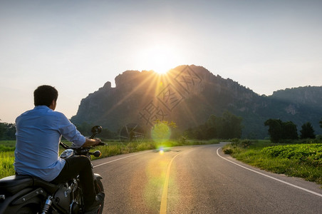 户外骑摩托车的手在通往山顶的路上日落和乌合之力的闪耀路通向山旅行运输图片