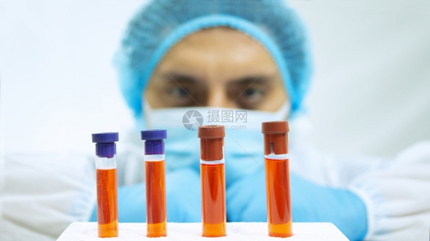 药物身穿生防护服面罩和蓝色手套的拉丁医生特写视图眼睛盯着一组4个玻璃试管白色背景上有红液体白背景上有红液体的管子技术研究图片