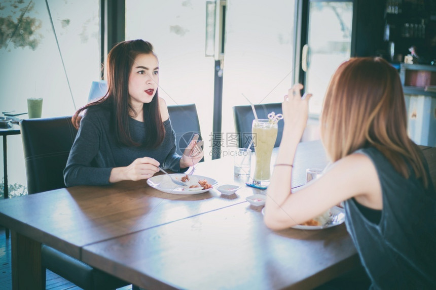 水平的购物吃两位年轻女朋友在餐厅一起欢笑和共进午餐图片