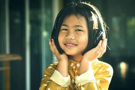 听力亚裔儿童在头部电话里听到音乐的肖像微笑着快乐的情感脸年轻图片