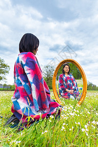 雨披成人户外年轻的哥伦布女青年在开花的牧场上与镜子坐在一起图片