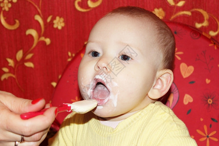 使满意吸引人的照顾幼小婴儿用童勺子喂养幼小婴儿红色的图片