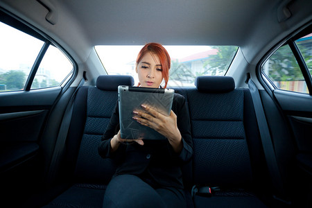 用平板电脑在车里的年轻商业女青药片司机座位出租车高清图片素材