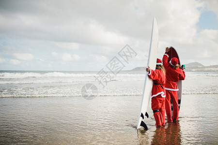 两个在海滩冲浪时打扮成圣诞老人的冲浪者女孩木板海洋图片
