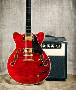 电子的褐色帆布背景上的红色半软形电吉他和放大器桃花心木头背景图片