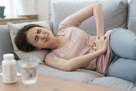 肚子月经期和疼痛的亚洲女在睡沙发上痛苦的年轻妇女在家中睡觉时抽筋淑女胃背景图片